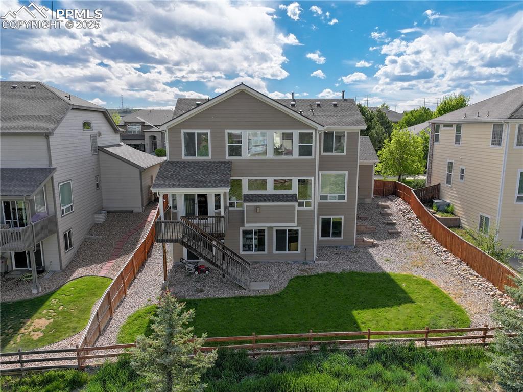 Caption: Rear view of house with stairs, a residential view, a fenced backyard, roof with shingles, and a dec