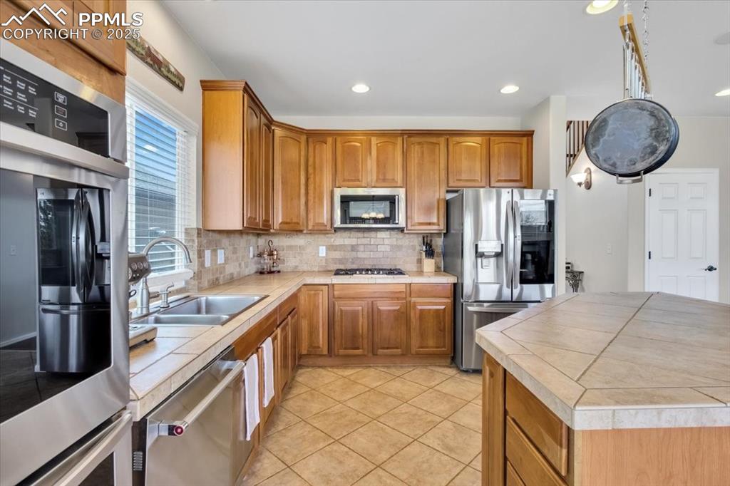 Image 12 of 30: Kitchen featuring tile countertops, stainless steel appliances, brown cabin