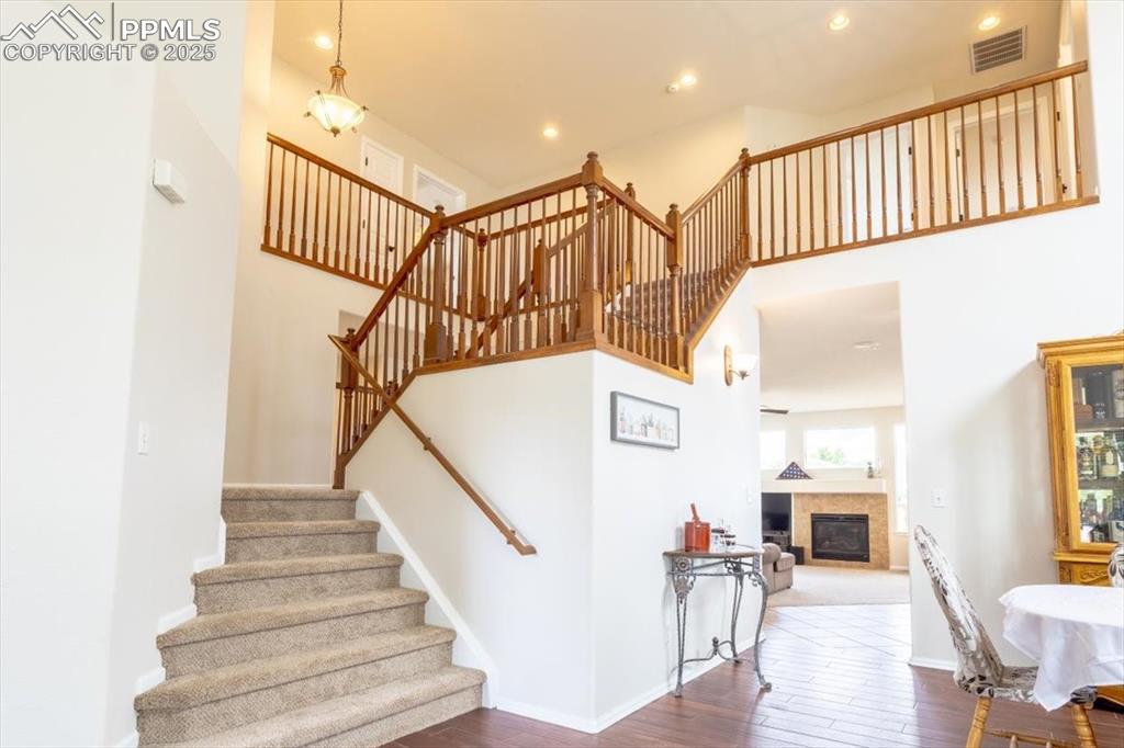 Image 3 of 30: Stairway featuring a towering ceiling, wood finished floors, a fireplace, a