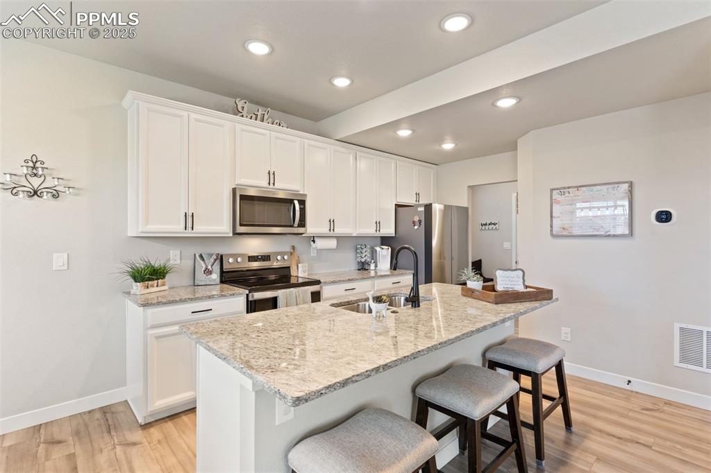 Image 8 of 26: Kitchen with stainless steel appliances, a kitchen bar, white cabinetry, li