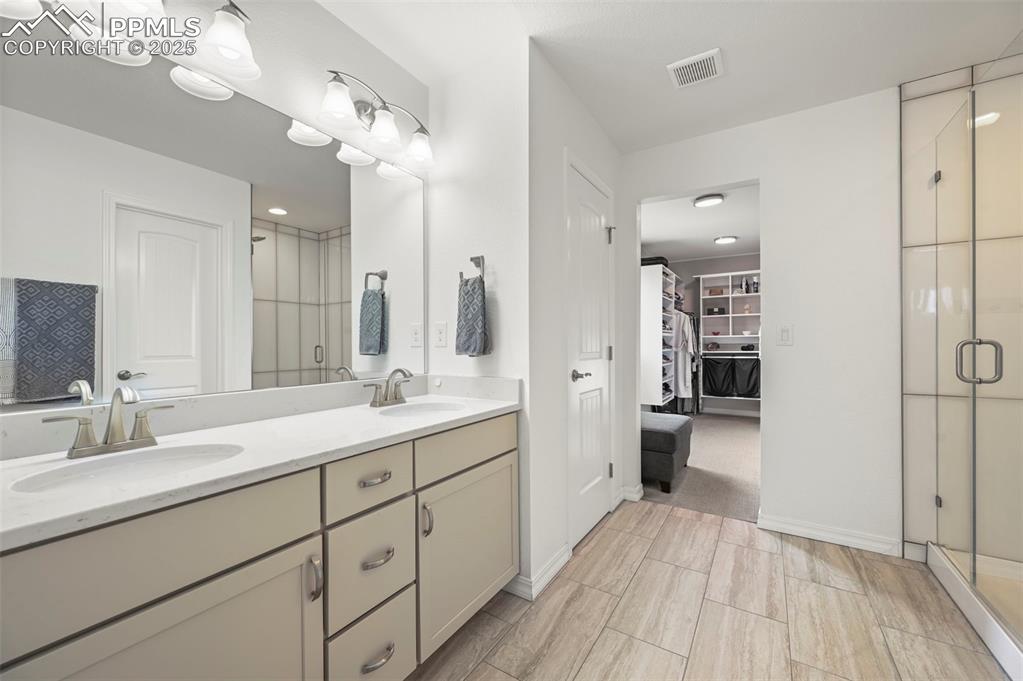 Image 19 of 50: Bathroom with double vanity, a shower stall, and a walk in closet