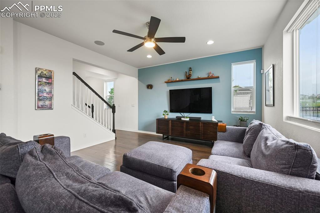 Image 5 of 50: Living room with dark healthy amount of natural light, stairs, ceiling fan,