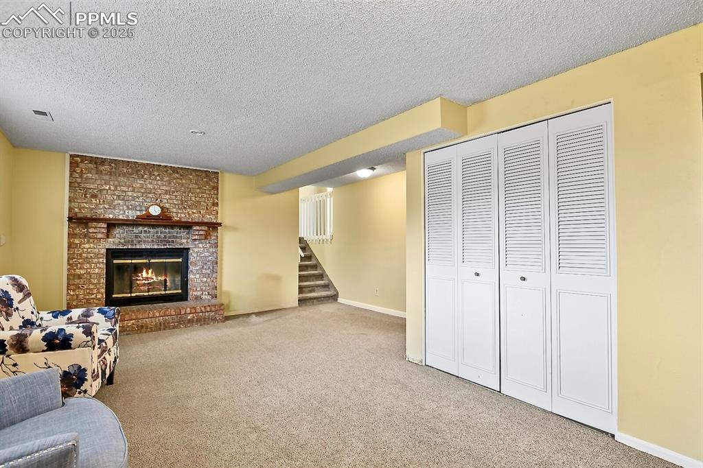 Image 13 of 17: Family room with carpet floors, stairway, a textured ceiling, and a firepla