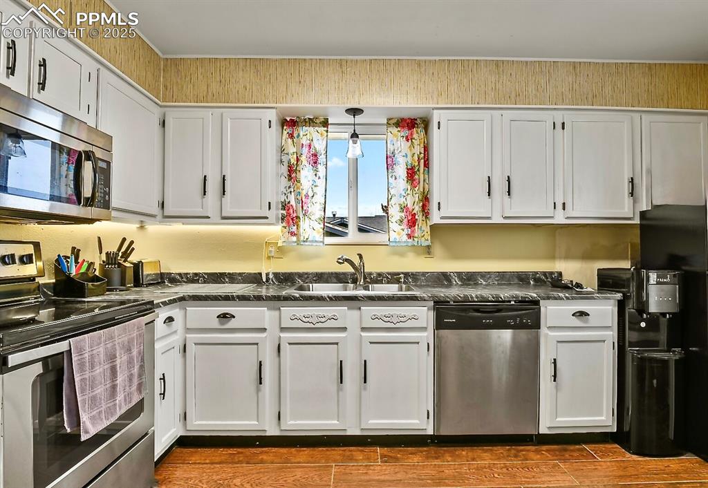 Image 8 of 17: Kitchen featuring stainless steel appliances, white cabinets, dark tile flo
