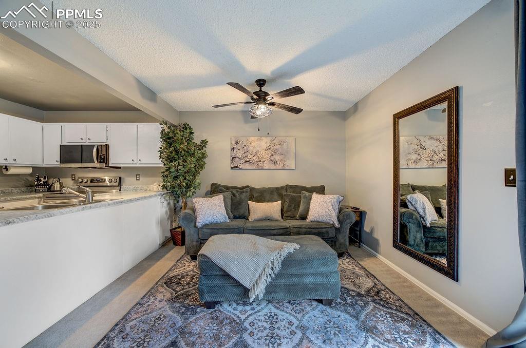 Image 13 of 48: Living room featuring ceiling fan, light carpet, and a textured ceiling