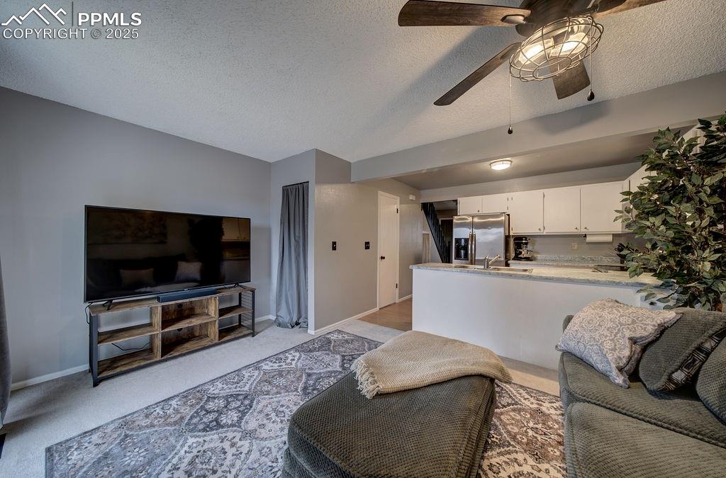Image 16 of 48: Living room with a ceiling fan, light carpet, and a textured ceiling