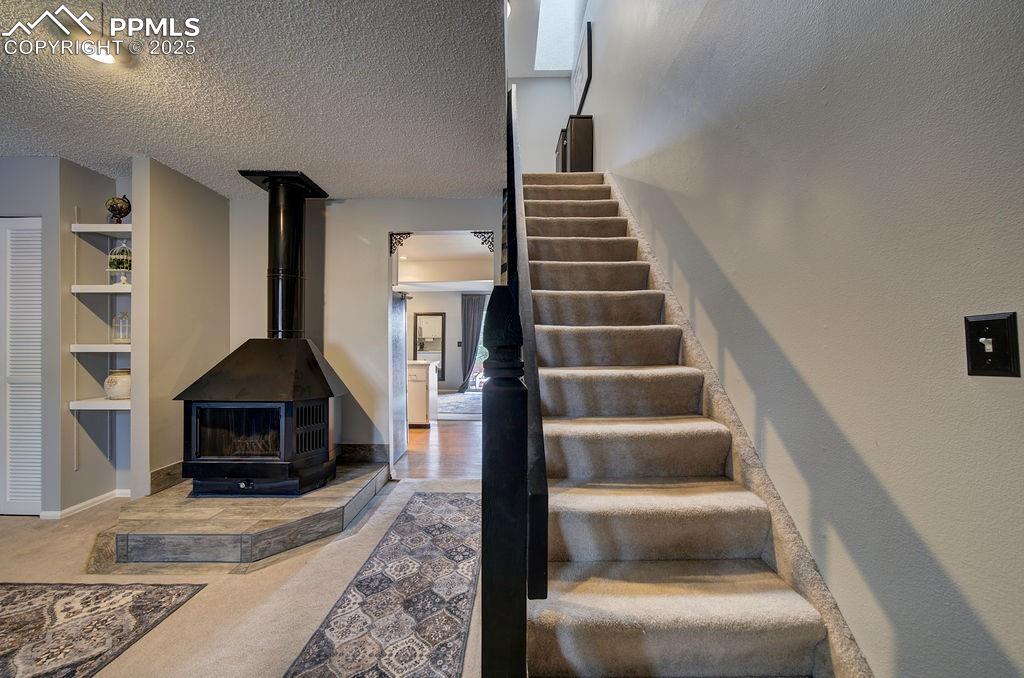 Image 25 of 48: Staircase with a textured ceiling, a wood stove, and carpet floors