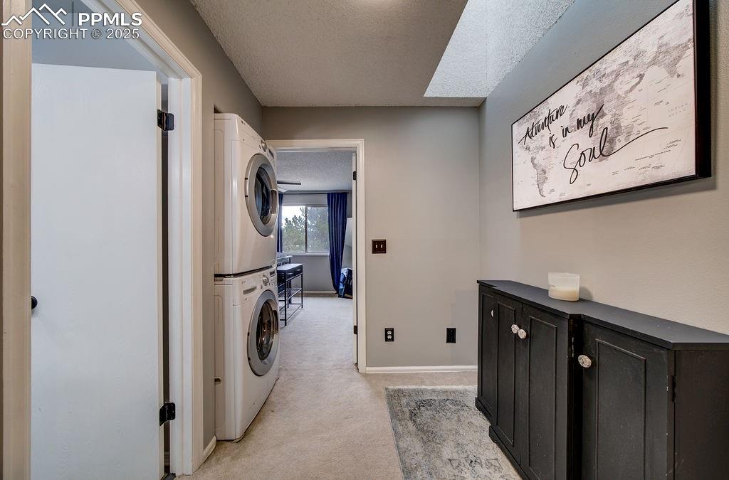Image 26 of 48: Laundry area featuring a textured ceiling, light colored carpet, and stacke