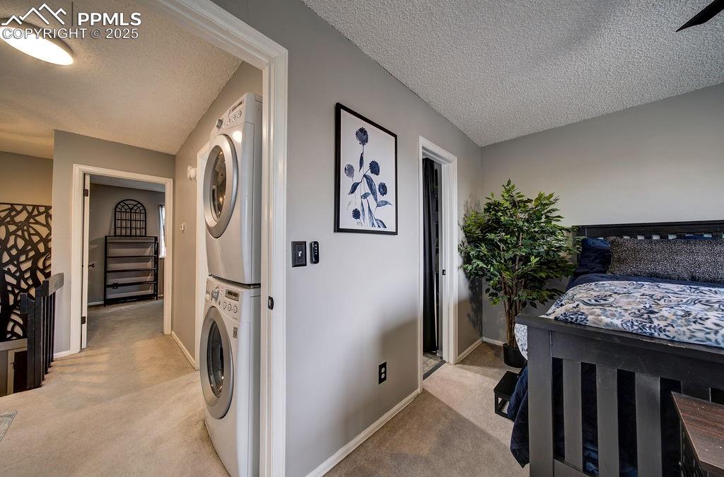 Image 36 of 48: Laundry room featuring a textured ceiling, light colored carpet, and stacke