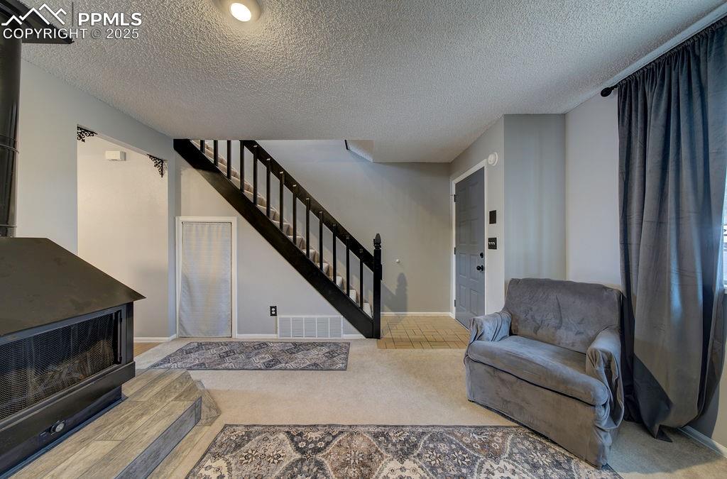 Image 41 of 48: Carpeted living area featuring a wood stove, a textured ceiling, and stairs