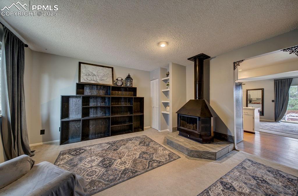 Image 43 of 48: Living room featuring a textured ceiling, a wood stove, and light carpet