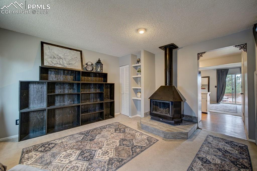 Image 6 of 48: Living area featuring light carpet, a textured ceiling, and a wood stove