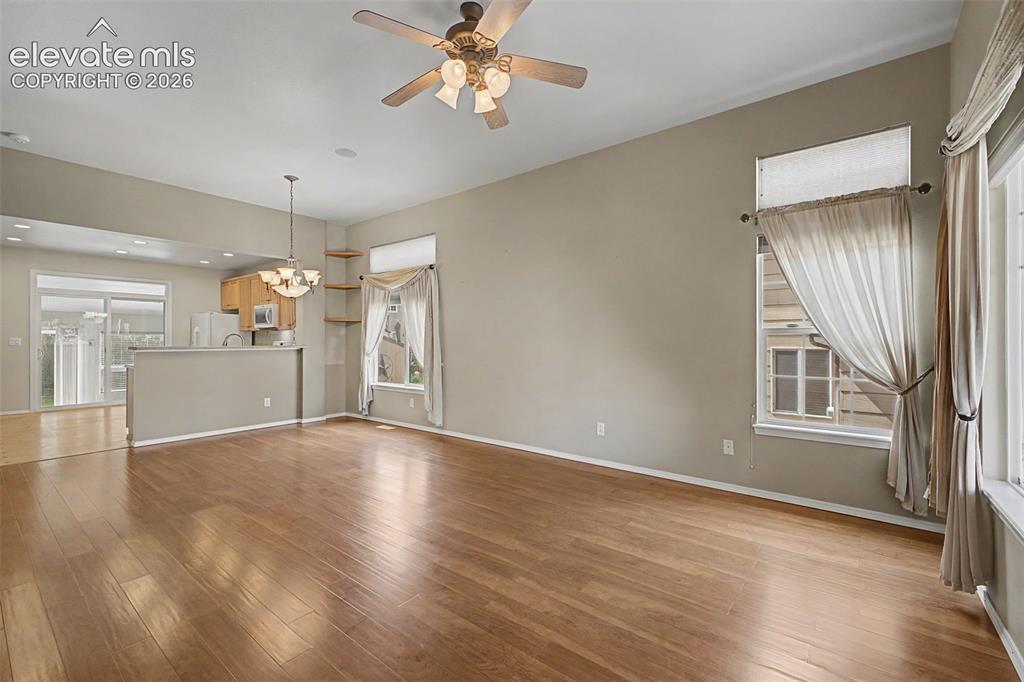 Image 10 of 49: Spacious living area featuring wood-finish flooring, a ceiling fan, and hig