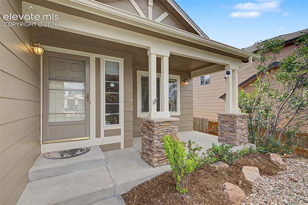 Image 5 of 49: Inviting covered front porch with stone-wrapped columns, complemented by a