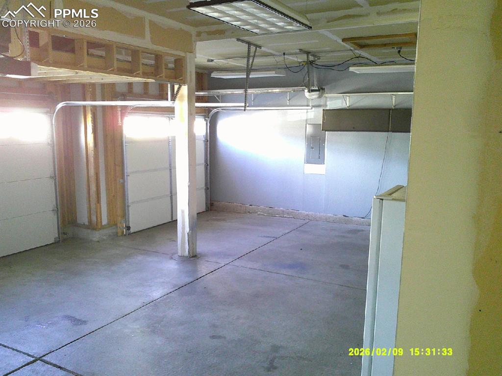Image 8 of 21: Garage with electric panel and freestanding refrigerator