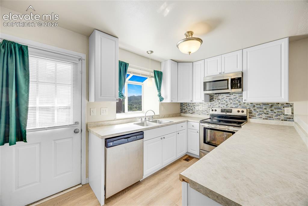Image 10 of 27: White cabinetry, stainless steel appliances, patterned tile backsplash, woo