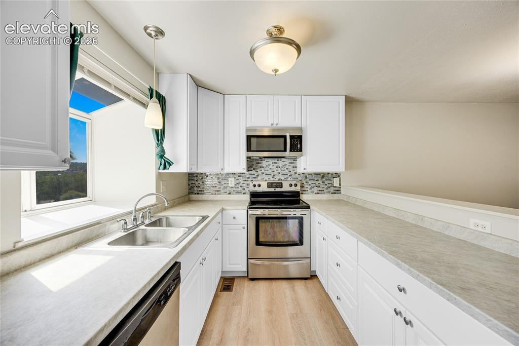 Image 11 of 27: White cabinetry, stainless steel appliances, mosaic tile backsplash, double