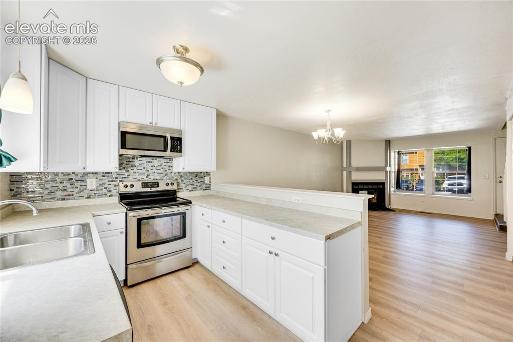 Image 12 of 27: Kitchen featuring white cabinetry, stainless steel appliances, mosaic tile