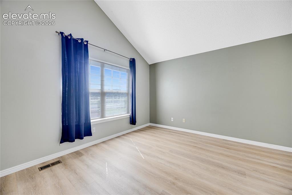 Image 15 of 27: Vaulted ceiling, wood-finish flooring, broad window, and neutral wall tones