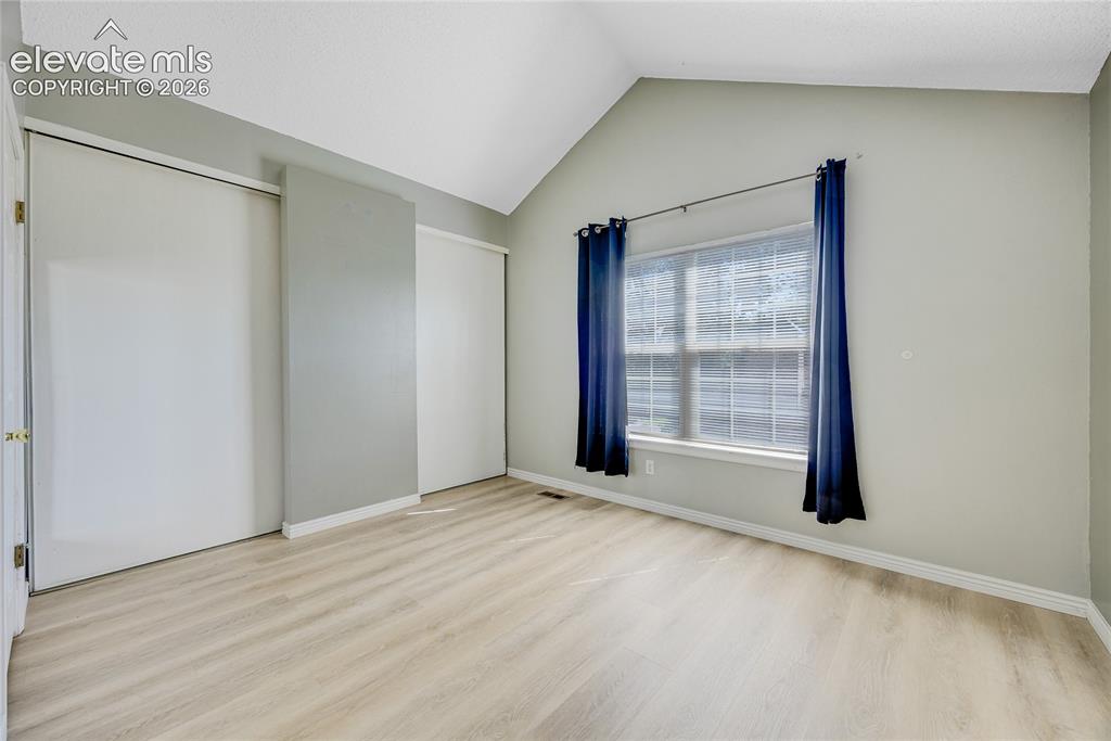 Image 16 of 27: Vaulted ceiling, two sliding closet doors, wood-finish flooring, and a wind