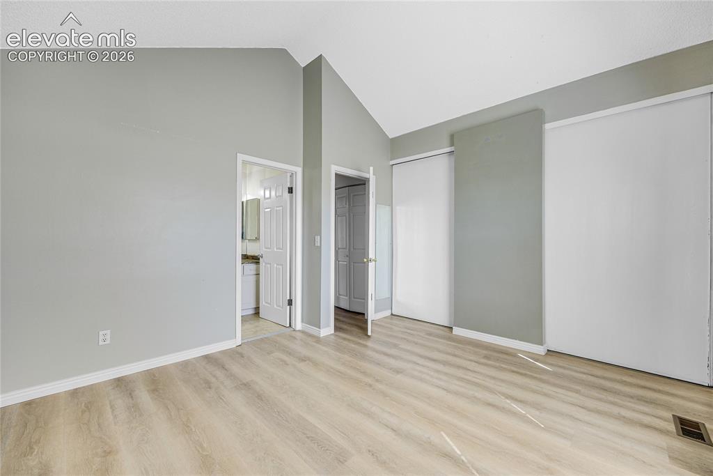 Image 17 of 27: Vaulted ceiling with light gray walls, wood-finish flooring, and white trim