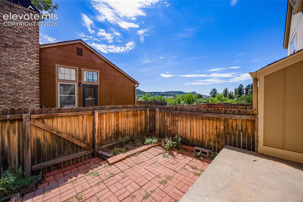 Image 24 of 27: Private brick paver patio with a wood privacy fence and concrete slab area