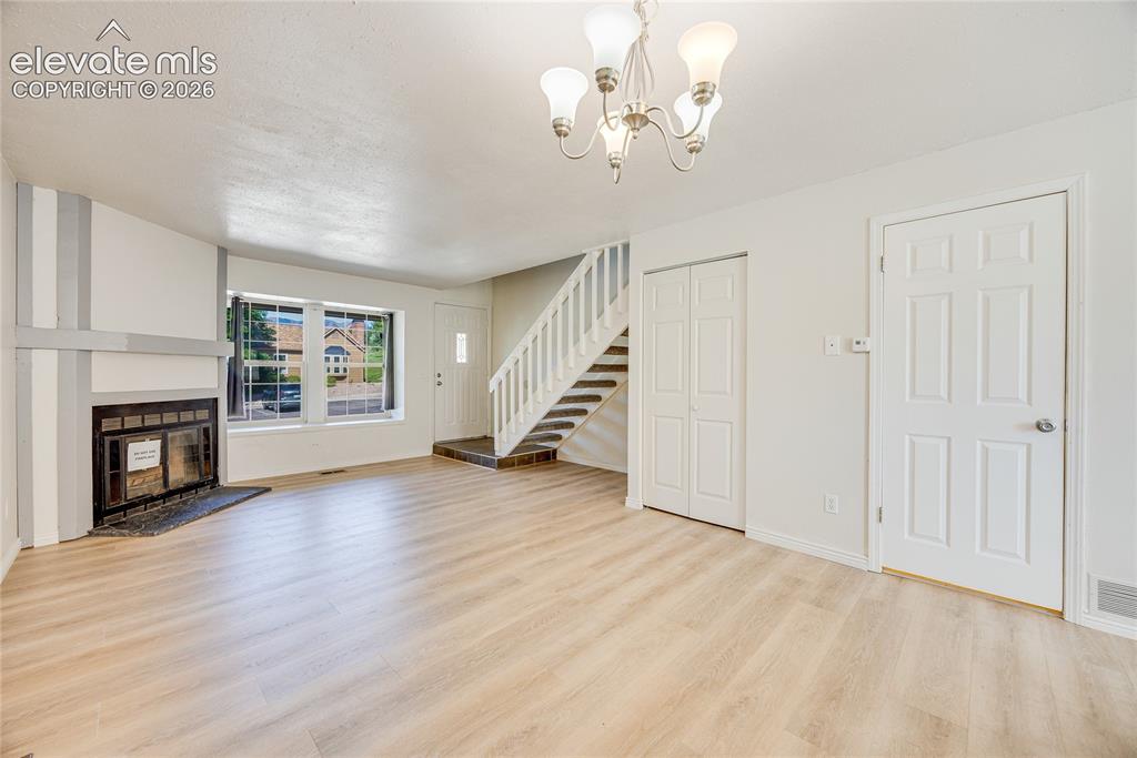 Image 8 of 27: Spacious living area featuring light wood-finish flooring, a fireplace with