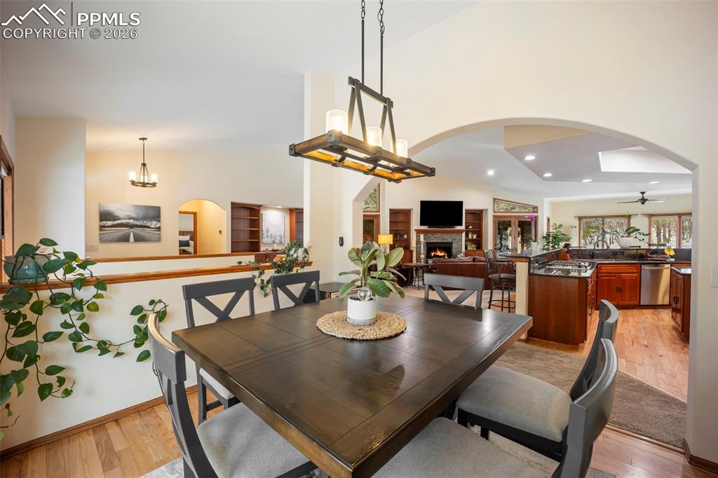 Image 17 of 48: Dining area with arched walkways, a warm lit fireplace, hardwood floors, hi