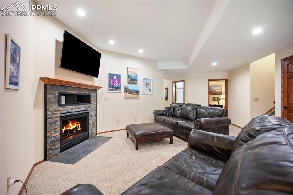 Image 27 of 48: Carpeted living area with a stone gas fireplace and recessed lighting