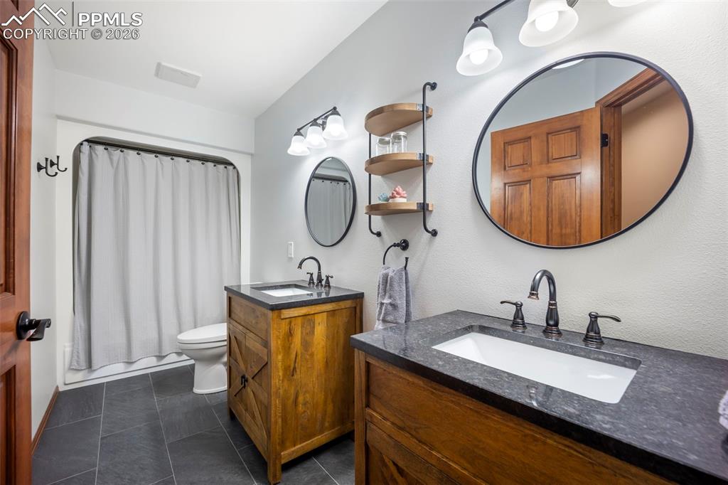Image 34 of 48: Bathroom featuring two vanities, dark tile patterned HEATED flooring, and s