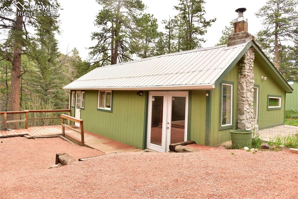 Caption: Back of property featuring french doors, a chimney, a wooden deck, and metal roof