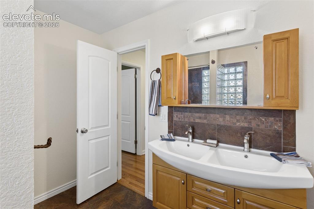 Image 26 of 50: Double vanity with dual basin sink, wood-finish cabinetry, and dark tiled b