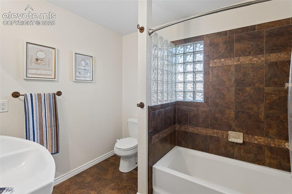 Image 29 of 50: White bathtub with brown tile surround and glass block window