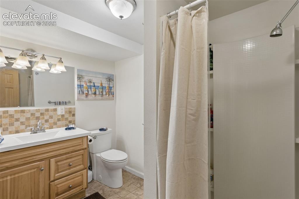 Image 38 of 50: Vanity with integrated sink, wood-finish cabinetry, and tiled backsplash