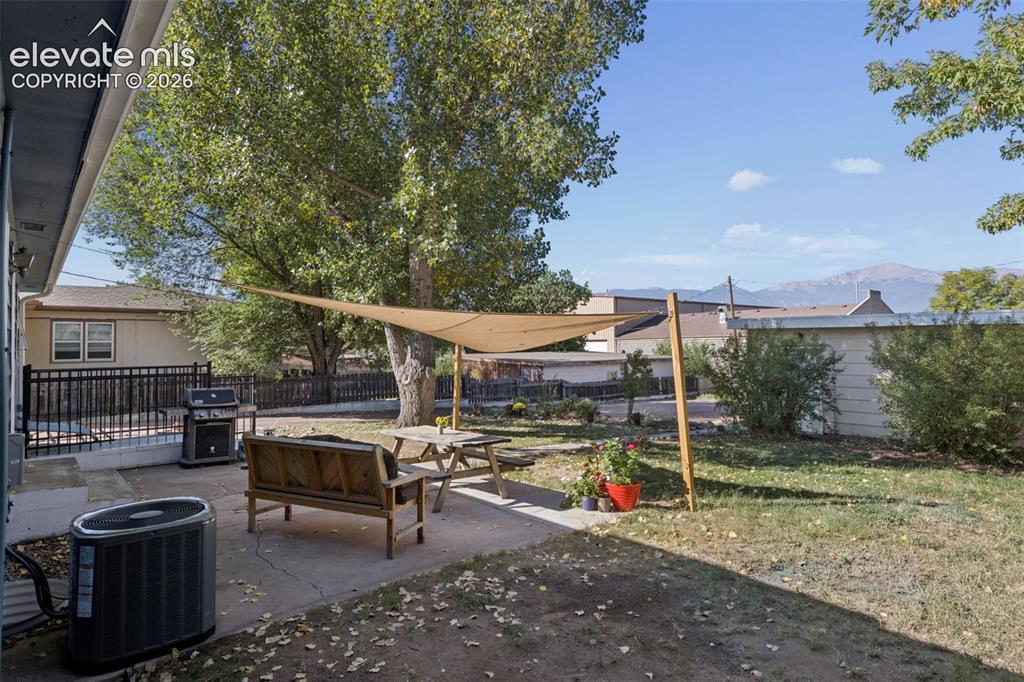 Image 44 of 50: Expansive backyard featuring a concrete patio, a shade sail, and mature tre