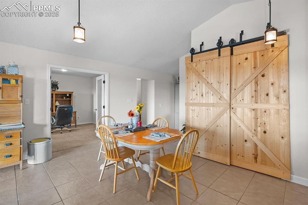 Image 13 of 39: Dining space with tile floors, a barn door, and vaulted ceiling