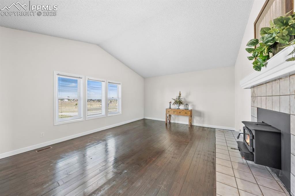Image 17 of 39: Living room featuring a wood stove, lofted ceiling and hardwood / wood-styl