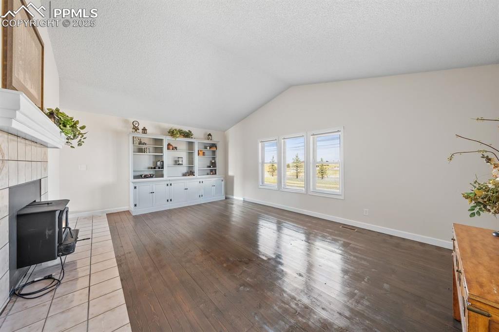 Image 18 of 39: Living room with lofted ceiling, dark wood-style flooring and a wood stove.