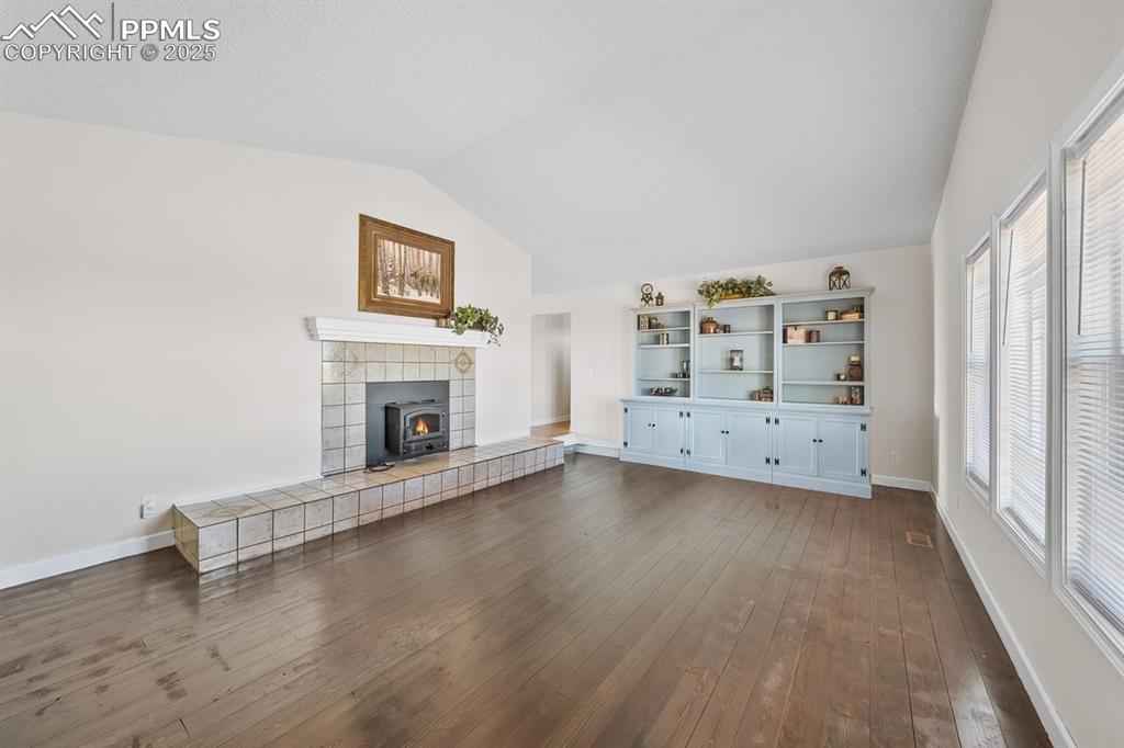 Image 4 of 39: Living room with vaulted ceiling, wood floors and wood stove