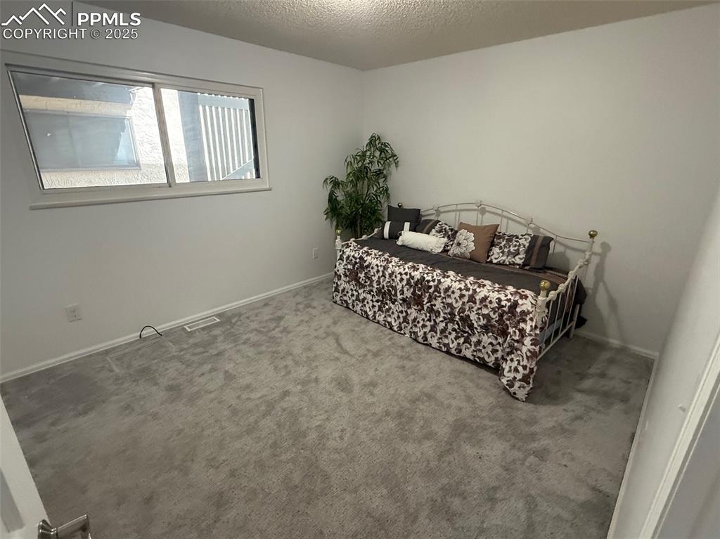 Image 8 of 11: Carpeted bedroom with a textured ceiling and baseboards