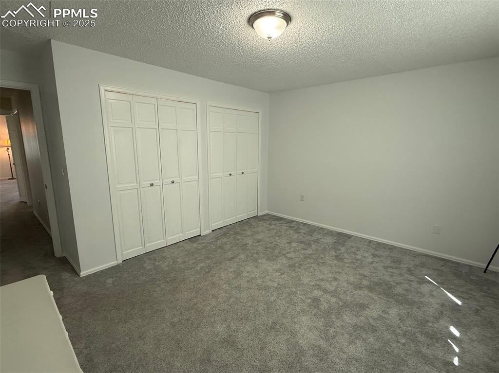 Image 9 of 11: Unfurnished bedroom with two closets, dark carpet, and a textured ceiling