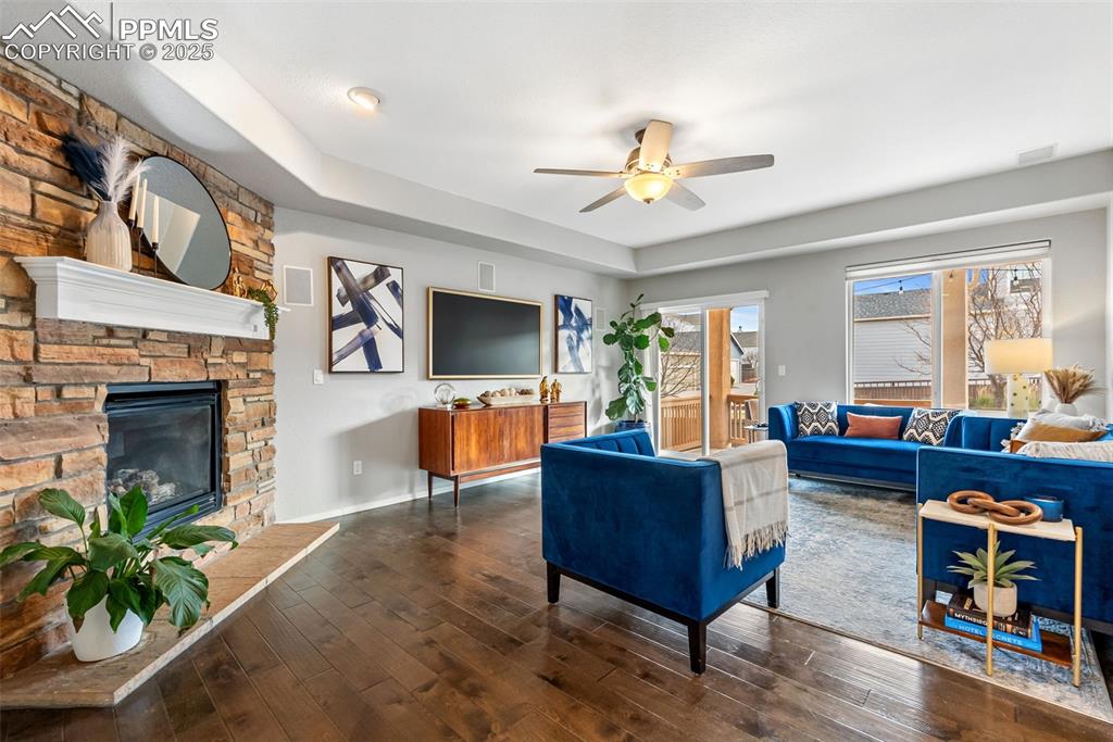 Image 11 of 50: Living area featuring wood-type flooring, a stone fireplace, ceiling fan, a