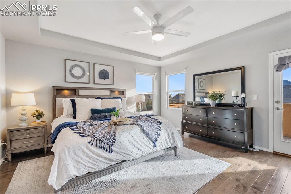 Image 21 of 50: Bedroom featuring a raised ceiling, wood finished floors, a ceiling fan, an