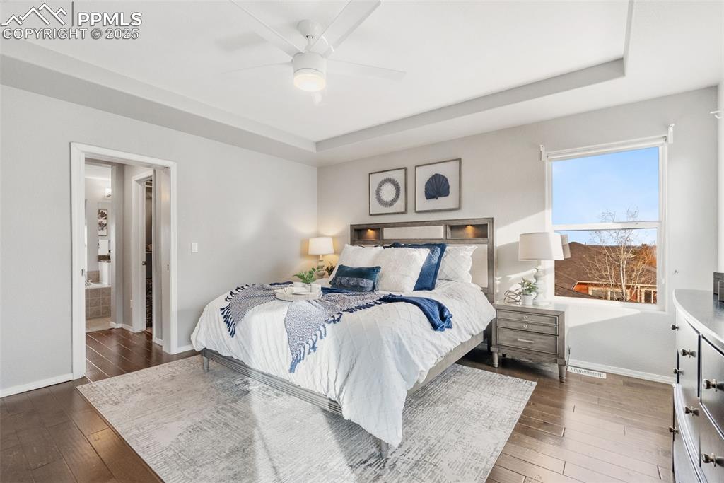 Image 22 of 50: Bedroom featuring a tray ceiling, ceiling fan, and dark wood-style flooring