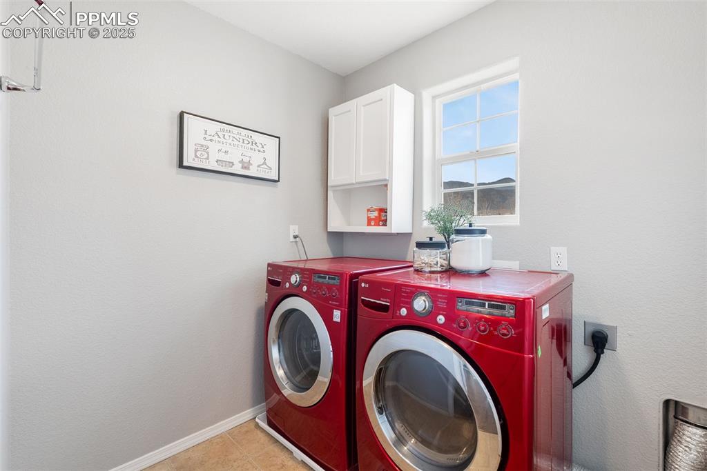 Image 32 of 50: Laundry area with cabinet space, washer and dryer, light tile patterned flo