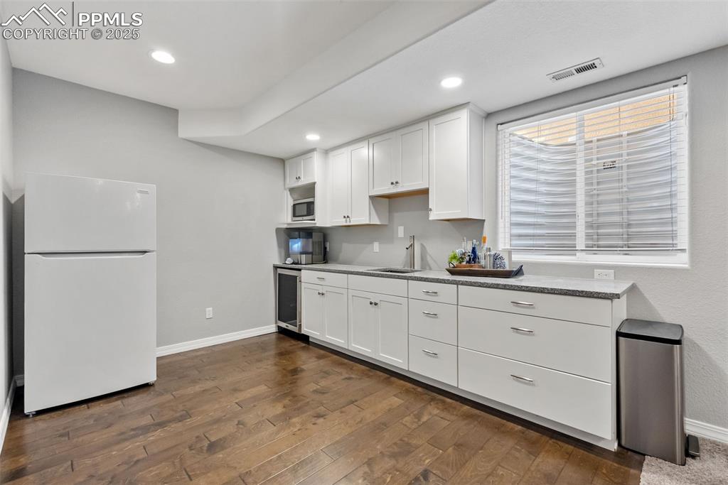 Image 35 of 50: Kitchen with white cabinetry, freestanding refrigerator, dark wood-style fl