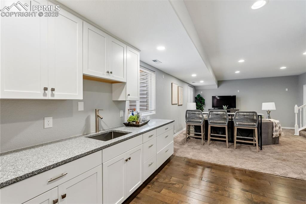 Image 36 of 50: Kitchen featuring white cabinets, dark wood-type flooring, light stone coun