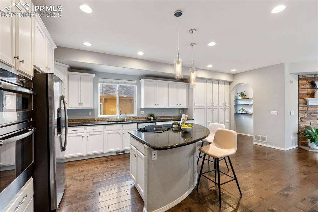 Image 8 of 50: Kitchen featuring a kitchen bar, stainless steel appliances, decorative lig