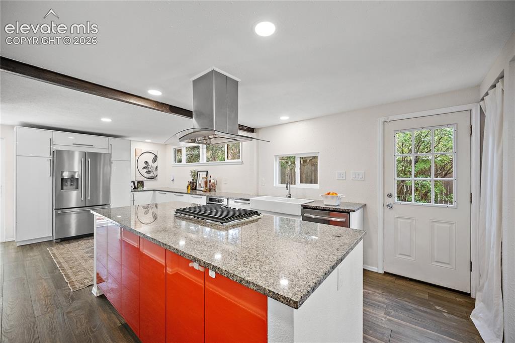 Image 15 of 41: Kitchen featuring a large island with a stone countertop and bright orange