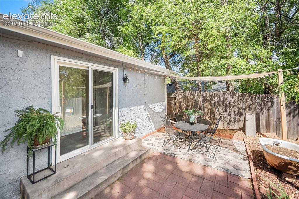 Image 32 of 41: Brick paver patio with a shade sail, bordered by a wooden privacy fence and